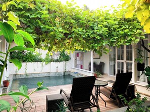 Un patio cubierto con piscina, mobiliario de mimbre y abundante vegetación.