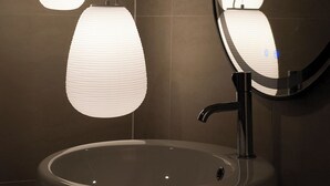 Een badkamer met een rond wastafel, een spiegel en twee hanglampen.