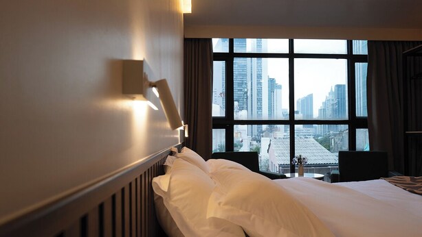 Een hotelkamer met een groot raam, een bed met witte lakens, een nachtkastje en een lamp.