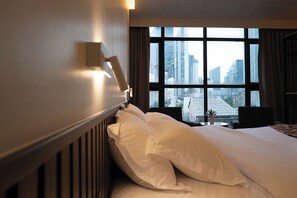Een hotelkamer met een groot raam, een bed met witte lakens, een nachtkastje en een lamp.