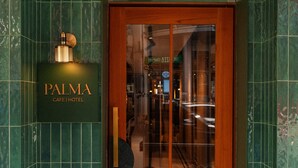 Een hotelentree met een geél groen betegelde gevel, een houten deur en een bord met de tekst 
