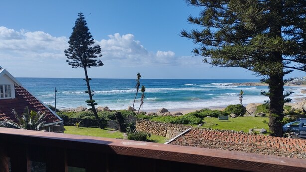 A coastal view from a balcony with a stone wall, a wooden deck, and a view of the ocean. - Billy Bay Cottage (Margate)