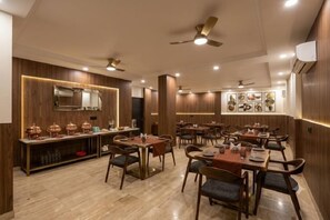 A restaurant with wooden paneling, multiple dining tables, and ceiling fans. - Hotel Sky View at Delhi IGI Airport (New Delhi)