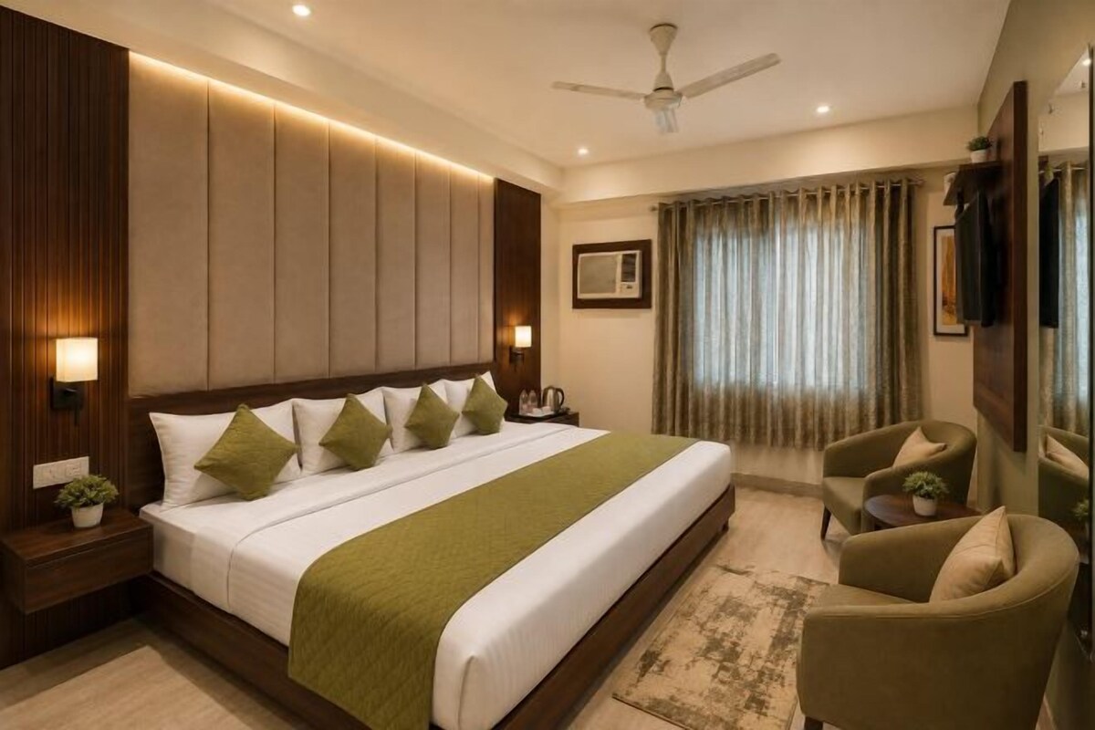 A hotel room with a large bed, a flat-screen TV, a ceiling fan, and a view of the outdoors through curtains.