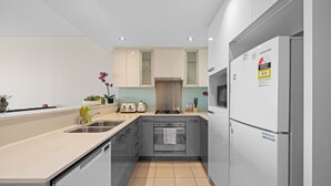Une cuisine moderne avec des meubles gris, un évier en acier inoxydable, un four encastré et un réfrigérateur Samsung.