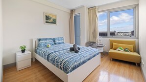 Une chambre à coucher comprenant un lit, une table de chevet, un petit canapé, une fenêtre avec vue et un luminaire au plafond.