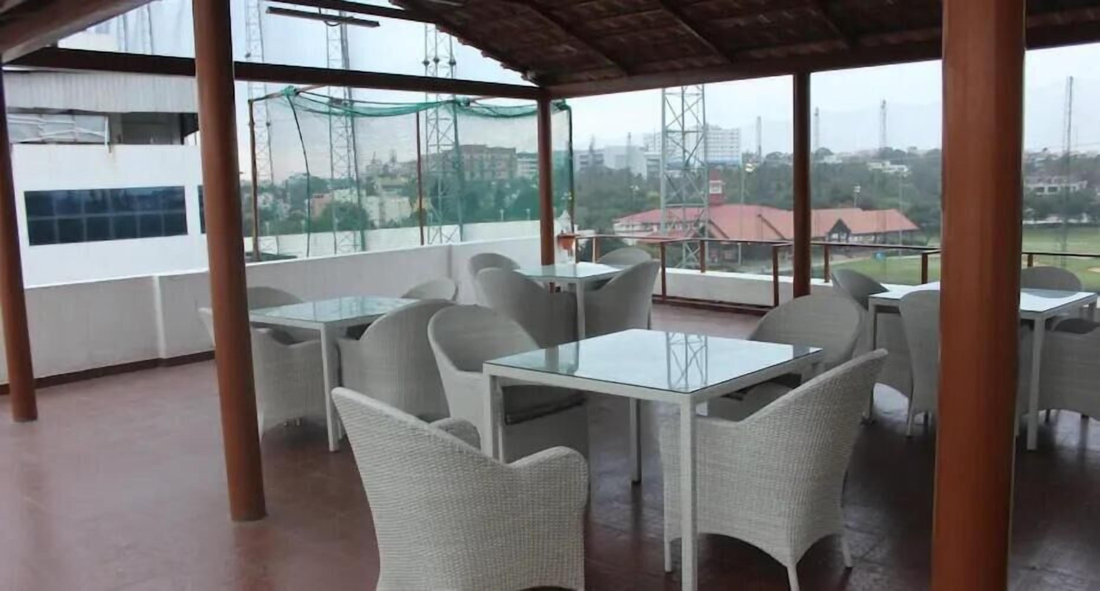 An outdoor seating area with tables and chairs, large windows, and a view of the cityscape.
