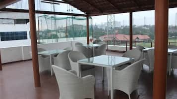 An outdoor seating area with tables and chairs, large windows, and a view of the cityscape.