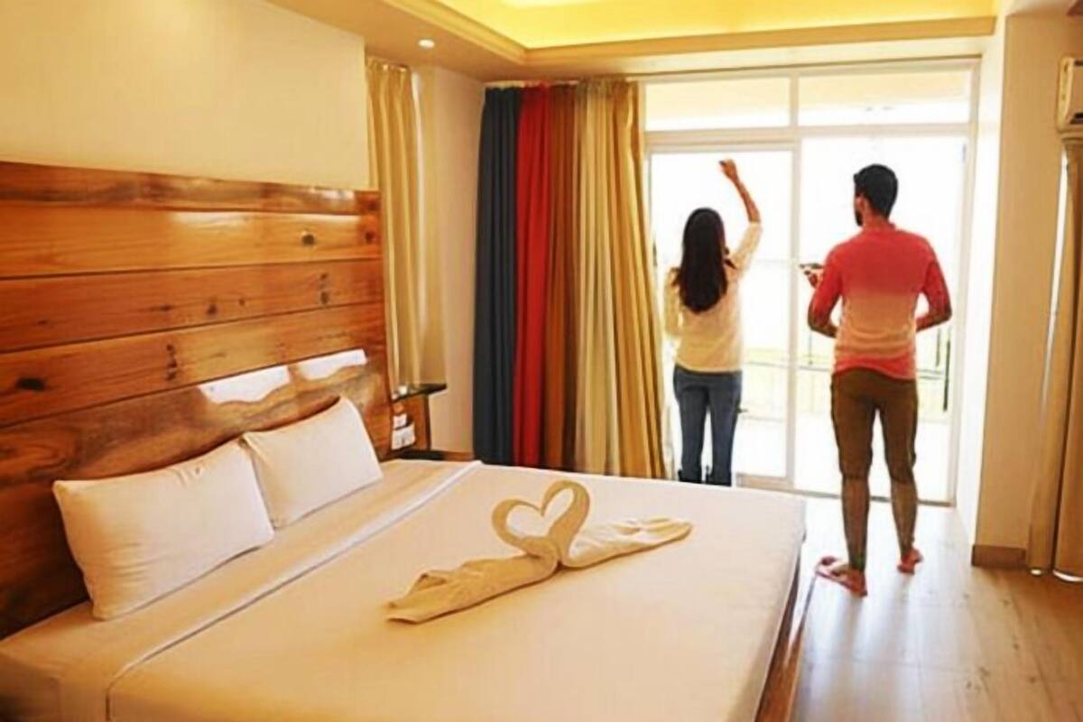 A hotel room with a wooden headboard, a bed with a heart-shaped towel, and a view of the outside through a sliding door.