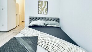 Un dormitorio moderno con una cama, un cuadro pequeño y un acceso a otra habitación.