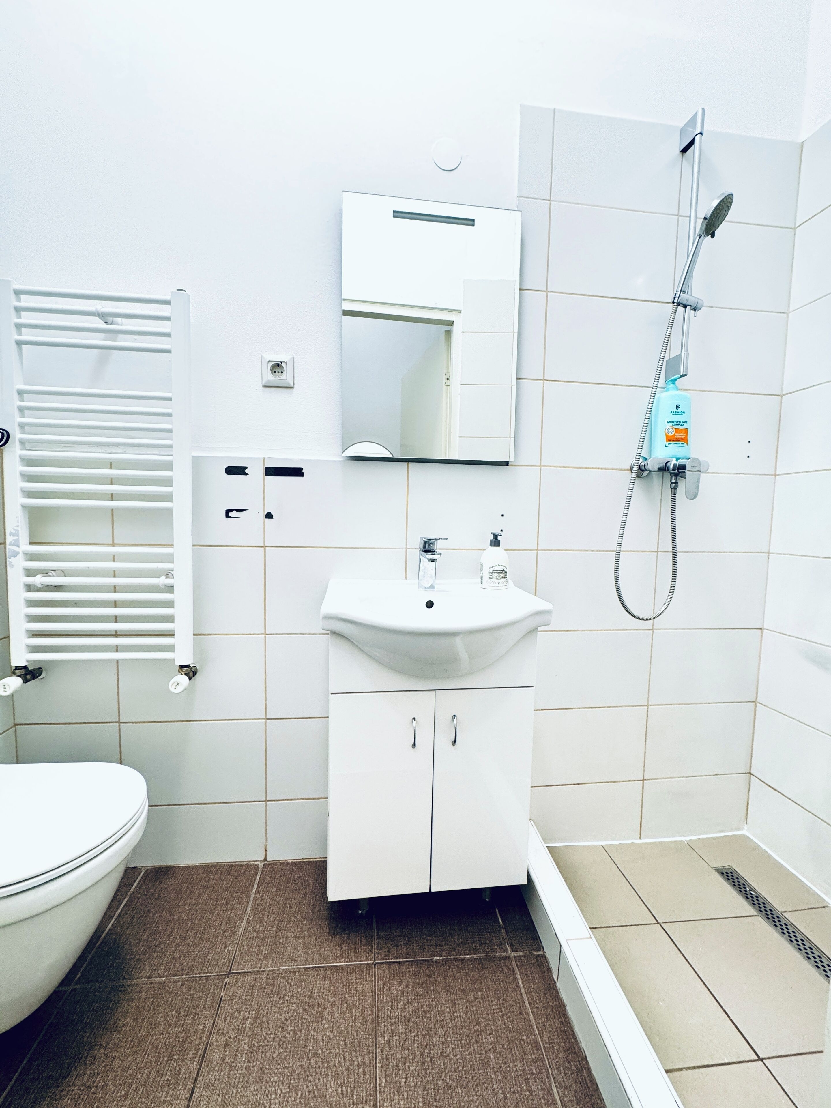 Une salle de bain comprenant des toilettes, un lavabo, un miroir, une douche et un porte-serviettes.