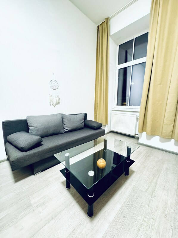 Una sala de estar moderna con un sofá gris, una mesa de centro de vidrio y una ventana con cortinas.