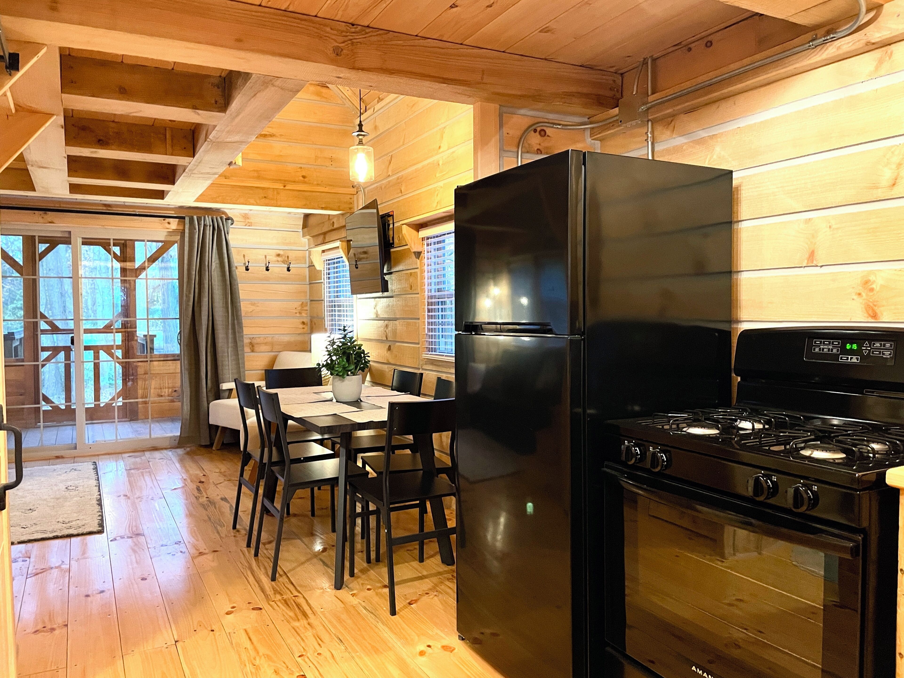 A wooden interior with a dining table, chairs, a black refrigerator, and a stove.
