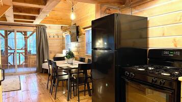 A wooden interior with a dining table, chairs, a black refrigerator, and a stove.