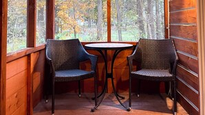 Eine Holzhütte mit zwei Korbstühlen und einem kleinen Tisch, großen Fenstern und Blick auf Bäume.