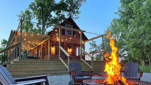 Eine Holzblockhütte mit Feuerstelle, Sitzgelegenheiten im Freien und einer überdachten Veranda.