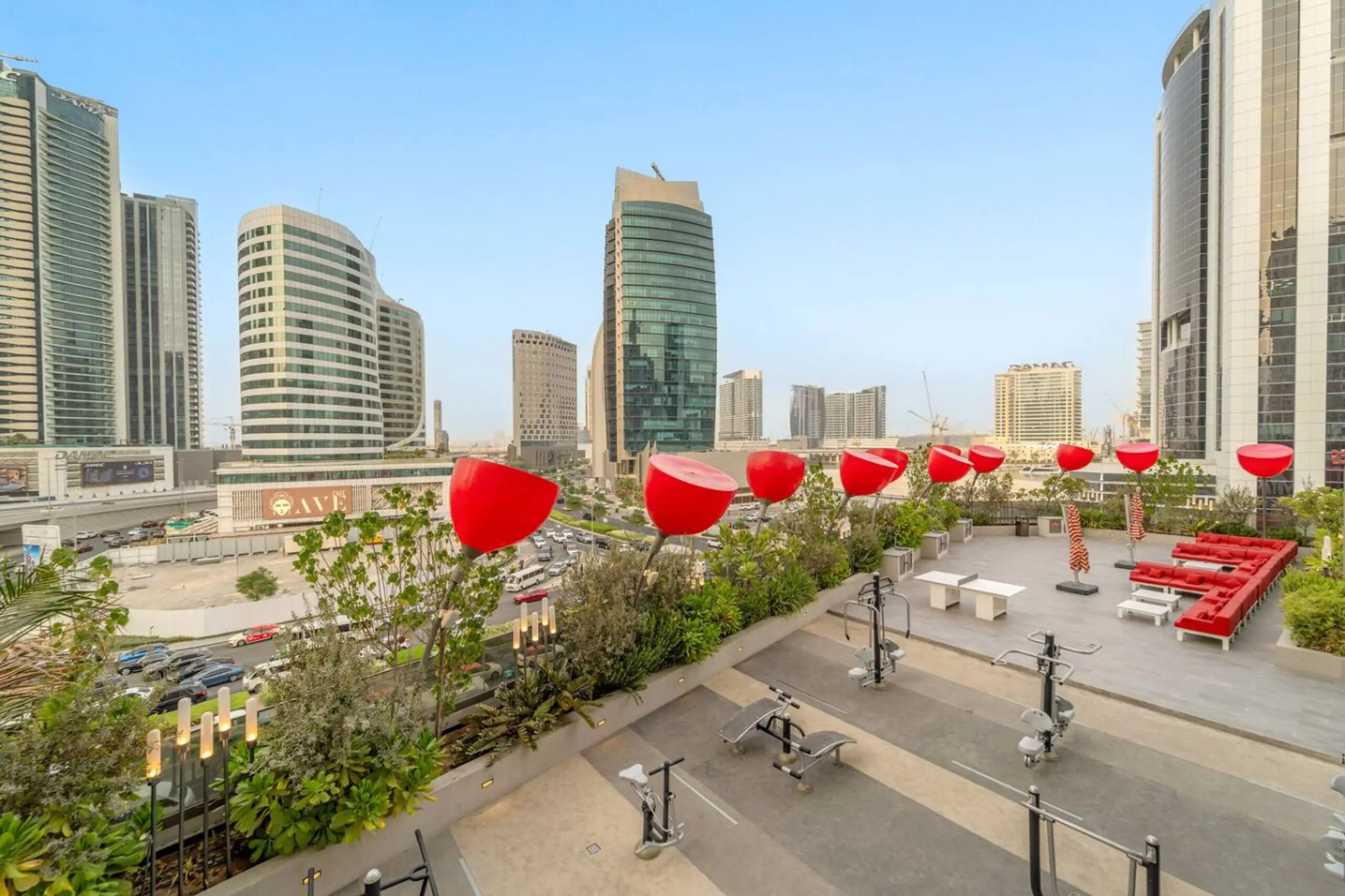 A rooftop terrace with exercise equipment, red spherical decorations, and a view of surrounding high-rise buildings.