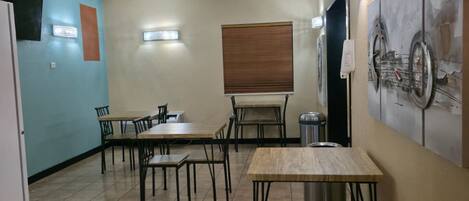 A dining area with tables and chairs, a window with blinds, and a wall-mounted bicycle artwork.