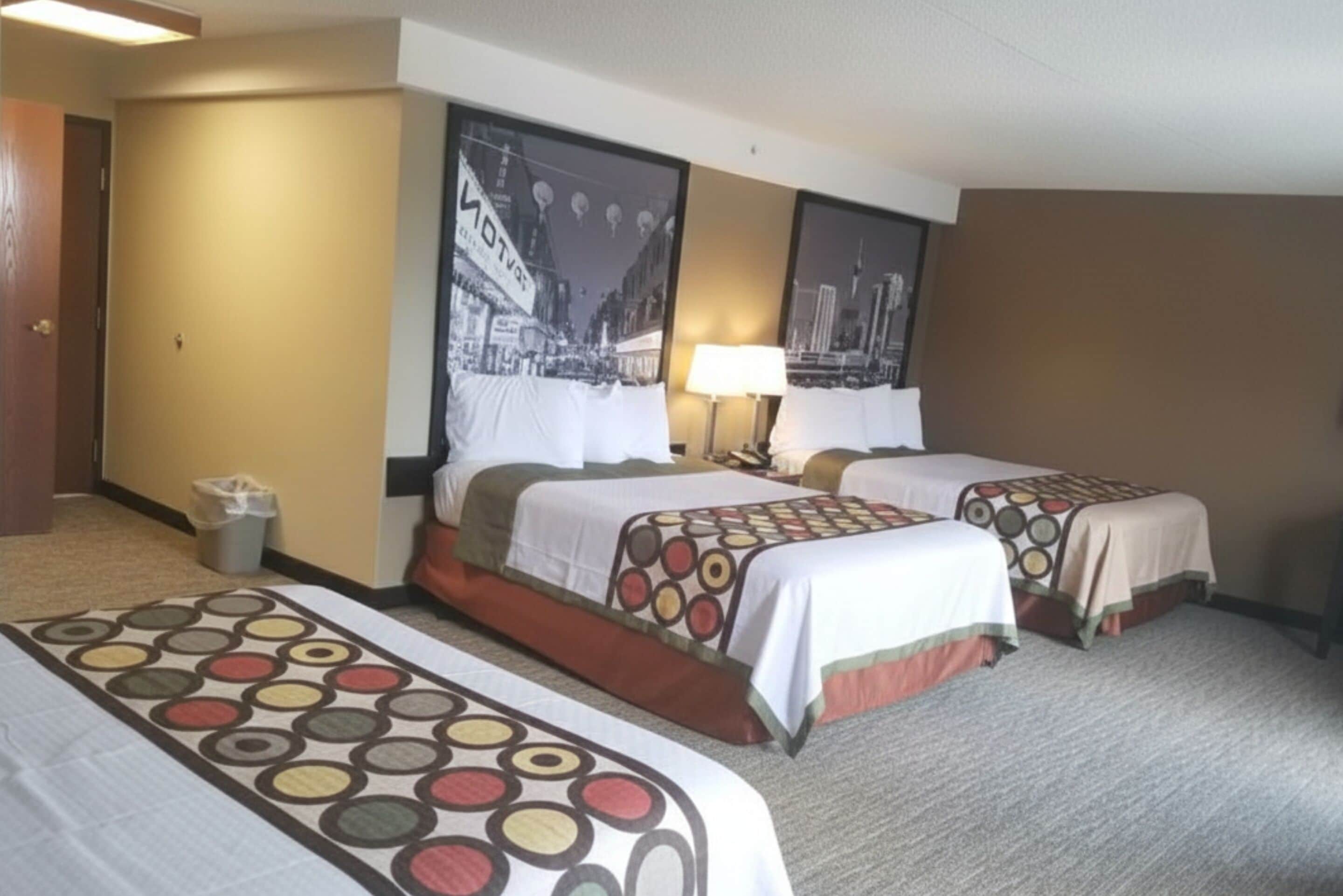 A hotel room with two beds, a trash bin, a lamp, and a wall-mounted picture.
