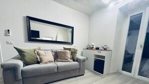 A modern living room with a grey sofa, a large mirror, a small table with a lamp, and a sliding glass door. - Romantic retreat with a private panoramic terrace near the Saturnia Hot Springs (Manciano)