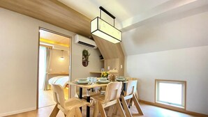 Ein Essbereich mit Holztisch und Stühlen, einer Hängelampe und Blick in ein Schlafzimmer durch eine offene Tür.