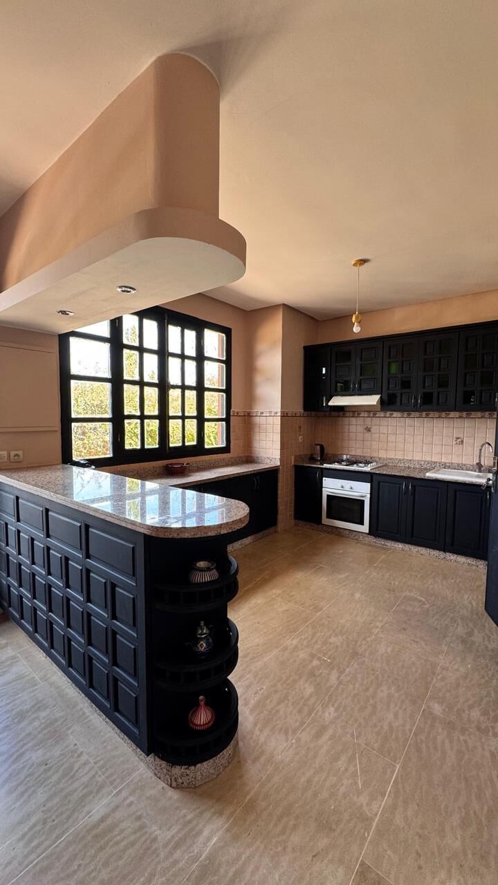 A modern kitchen with a large island, dark cabinetry, and a window providing natural light.