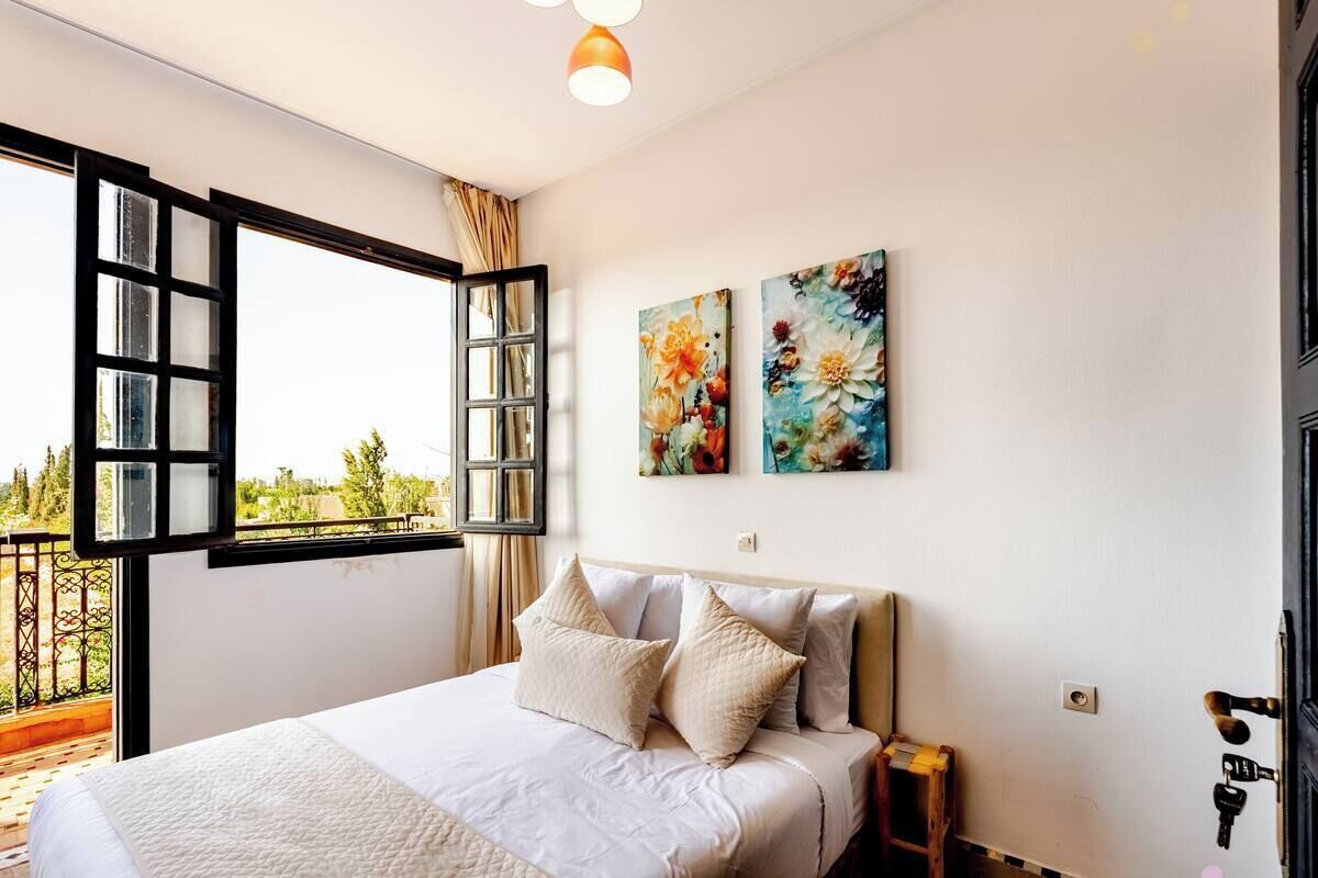 Ein Schlafzimmer mit einem Bett, einem Nachttisch, einem Fenster mit geöffnetem Klappladen und zwei Wandbildern.