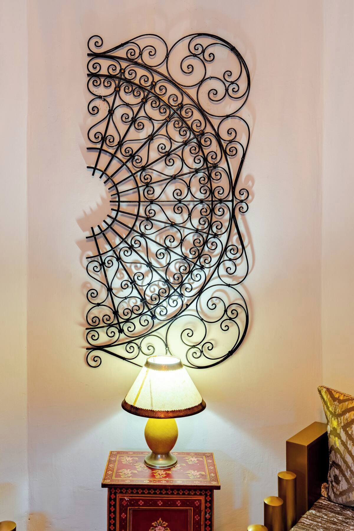 En dekorativ metallskulptur som hänger på väggen, med en lampa placerad på ett bord nedanför.