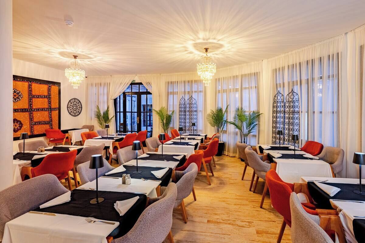 A dining area with tables set for multiple guests, chandeliers, and large windows with curtains.