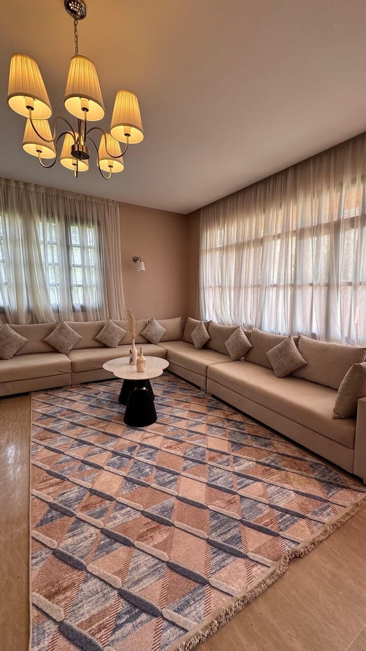 A living room with a sectional sofa, a patterned rug, and a chandelier.