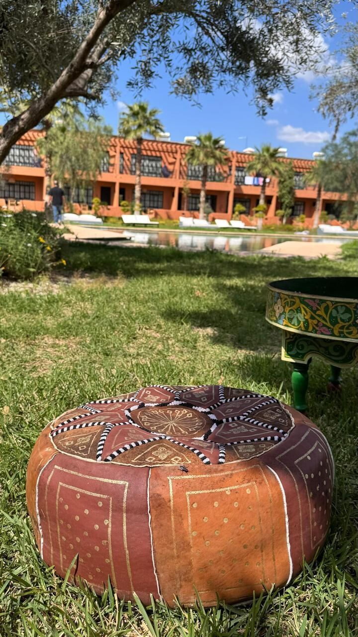 A round, ornately decorated ottoman on grass with a building in the background.