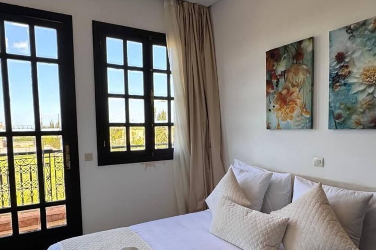 A bedroom with a large bed, two windows, and a painting on the wall.