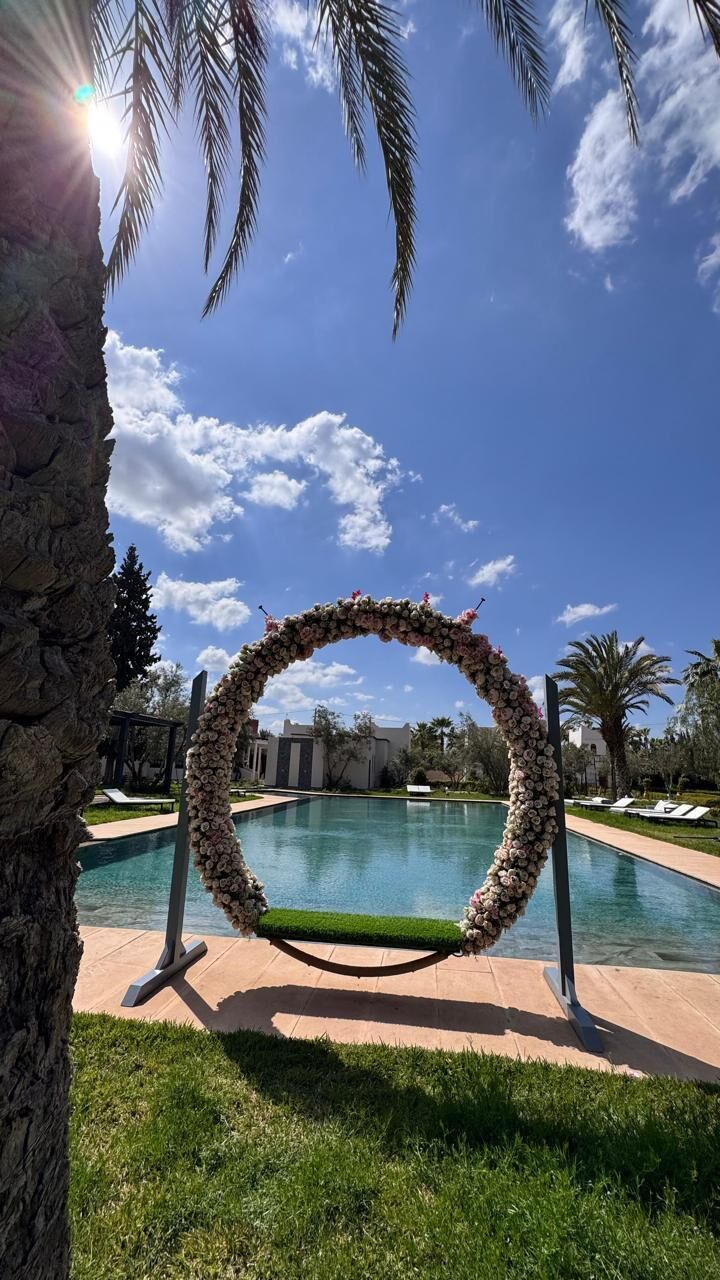 Une piscine agrémentée d’une arche fleurie, avec un ciel dégagé et des palmiers.