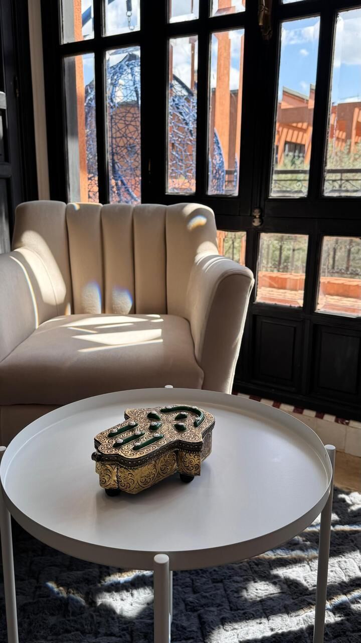 A room with a round table, a beige sofa, and a view through large windows.