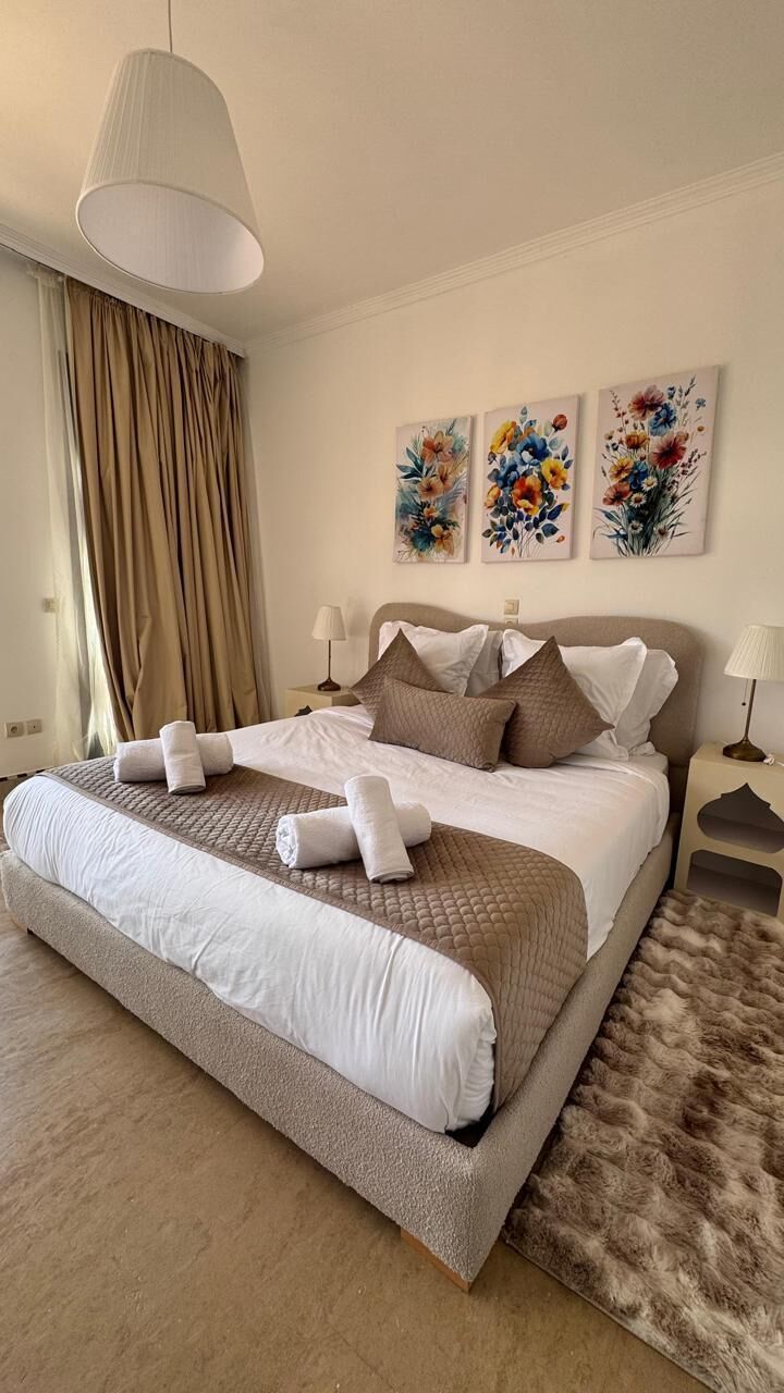 Ein Hotelzimmer mit einem großen Bett, zwei Nachttischen, einer Hängelampe und floraler Dekoration an der Wand.