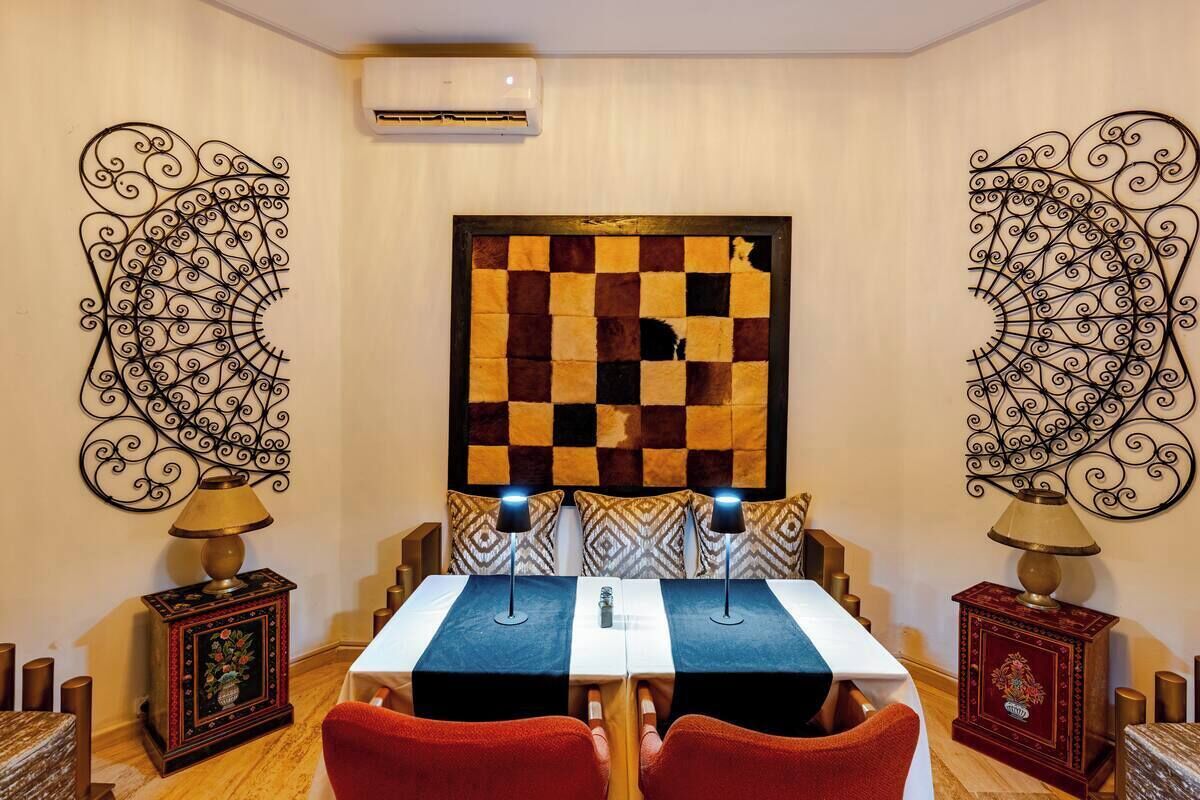 A dining area with a checkered tablecloth, two chairs, patterned wall decor, and a wall-mounted air conditioner.
