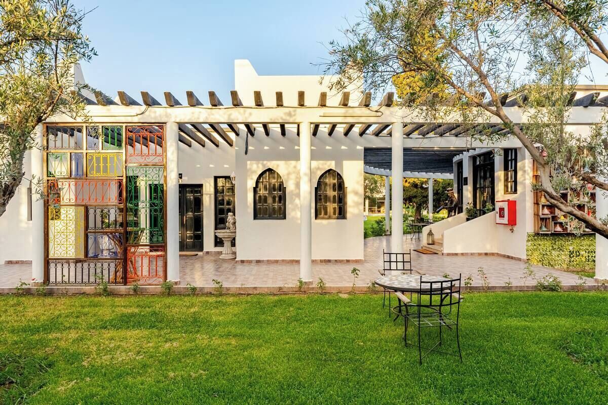 A white building with a covered patio, arched windows, and a small outdoor seating area.