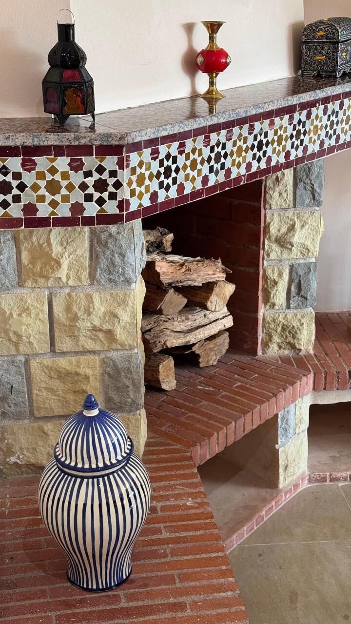 A fireplace with a mosaic-tiled mantel, a decorative vase, and a log storage area.