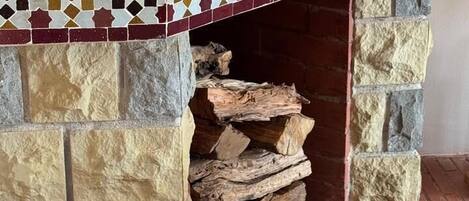 A fireplace with a mosaic-tiled mantel, a decorative vase, and a log storage area.