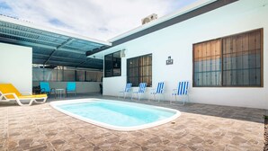 Una piscina con sillas de descanso y un porche cubierto.