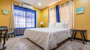 Habitación de hotel con una cama, un escritorio y una silla. Hay una ventana con cortinas azules y un cuadro en la pared.