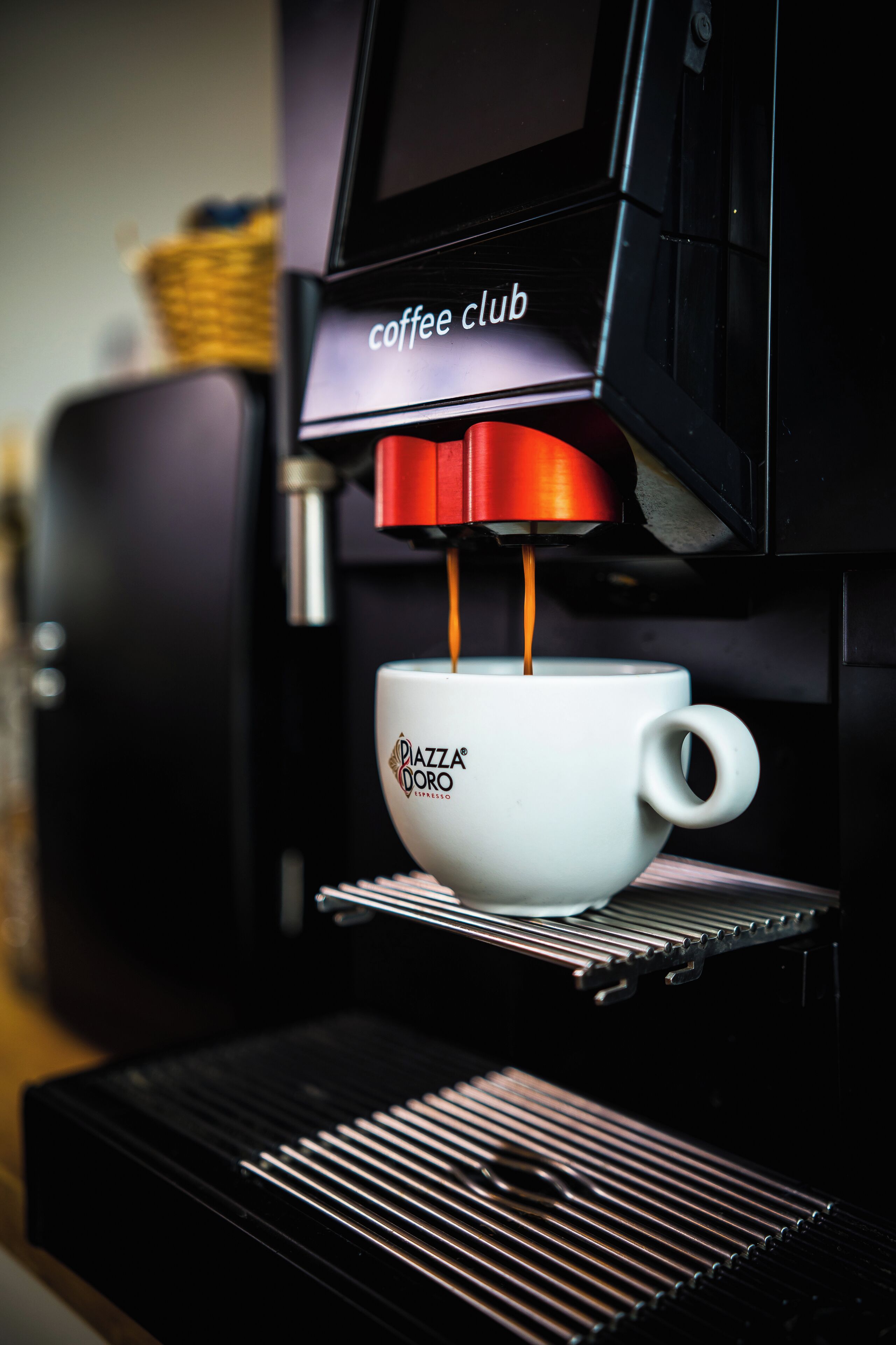 A coffee machine dispensing espresso into a white cup labeled "Piazza Dorca."