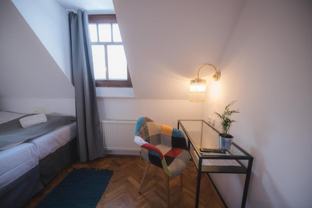Quarto pequeno e acolhedor com uma cama beliche, uma cadeira colorida, uma escrivaninha com abajur e um vaso com planta.