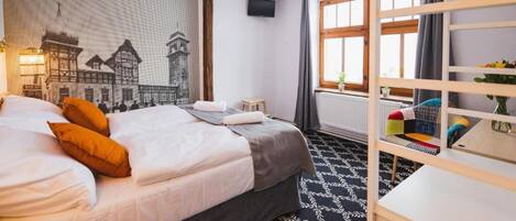 A hotel room with a bed, a TV, a window with curtains, a radiator, and a bookshelf.