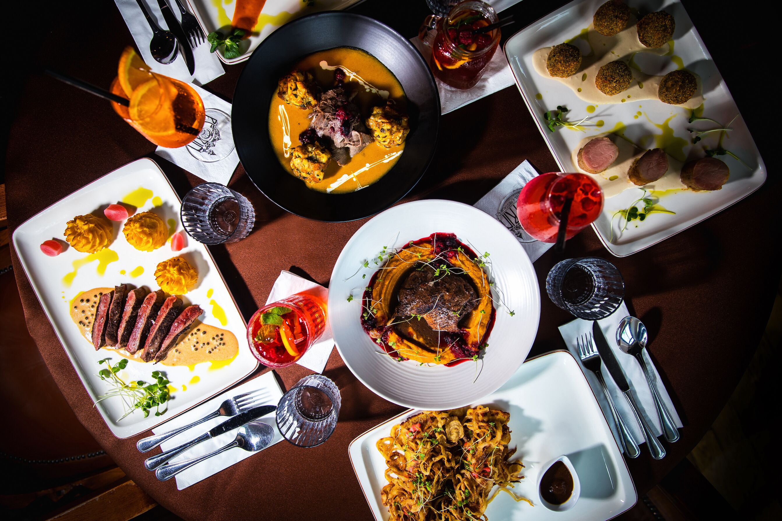 Diverse gerechten op een eettafel, waaronder een steak, een soepkom en verschillende borden met eten.