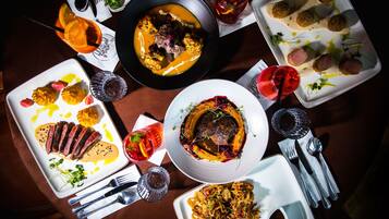 Diverse gerechten op een eettafel, waaronder een steak, een soepkom en verschillende borden met eten.