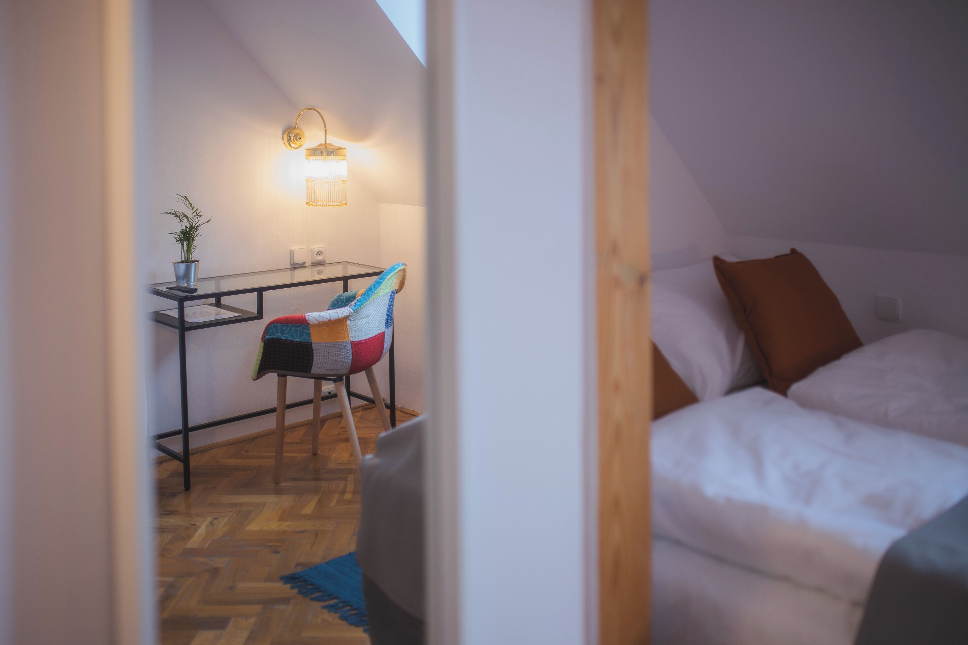 A cozy room with a bed, a desk with a chair, and a potted plant.