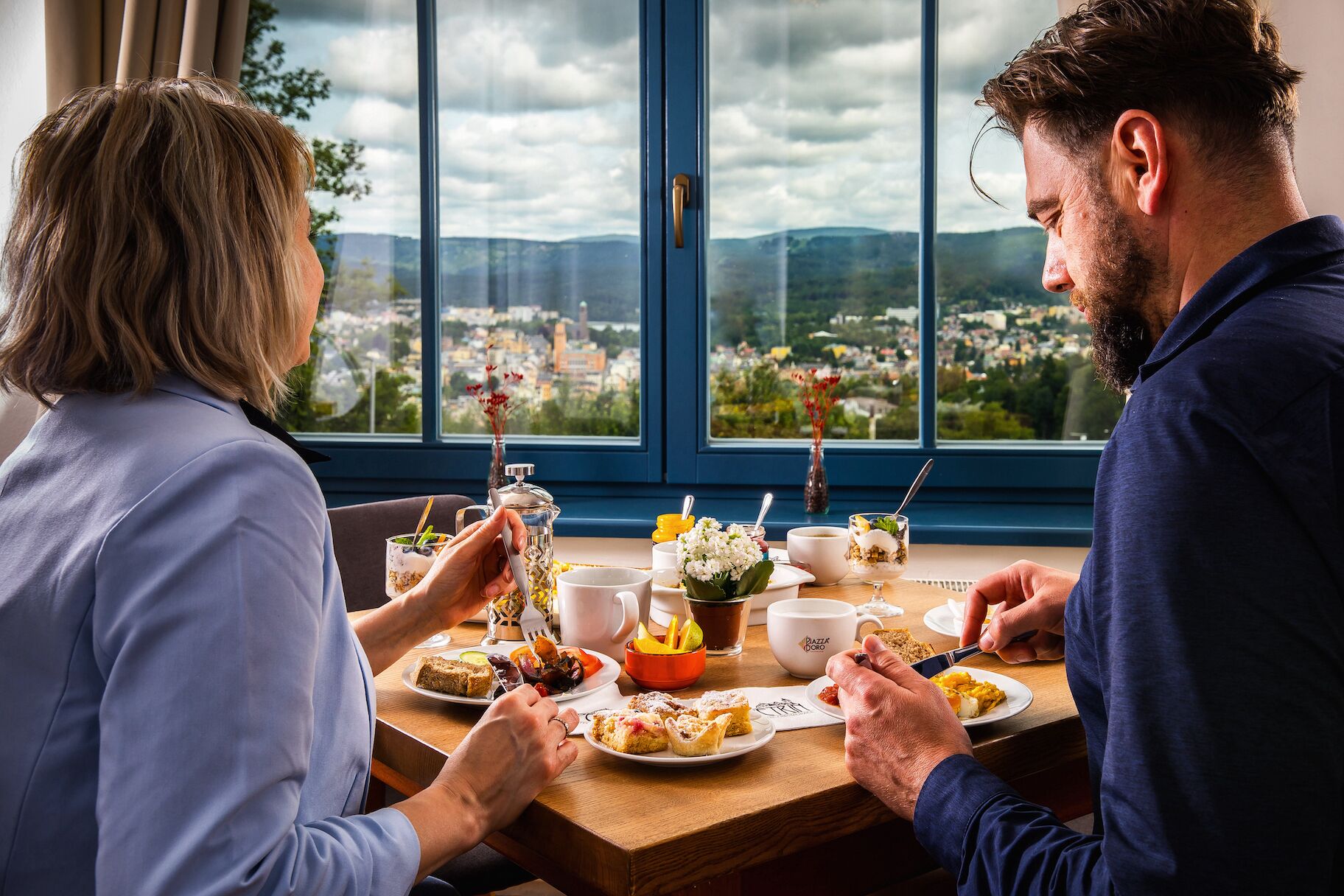 A couple dining at a table with a city view through large windows.