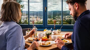 A couple dining at a table with a city view through large windows.