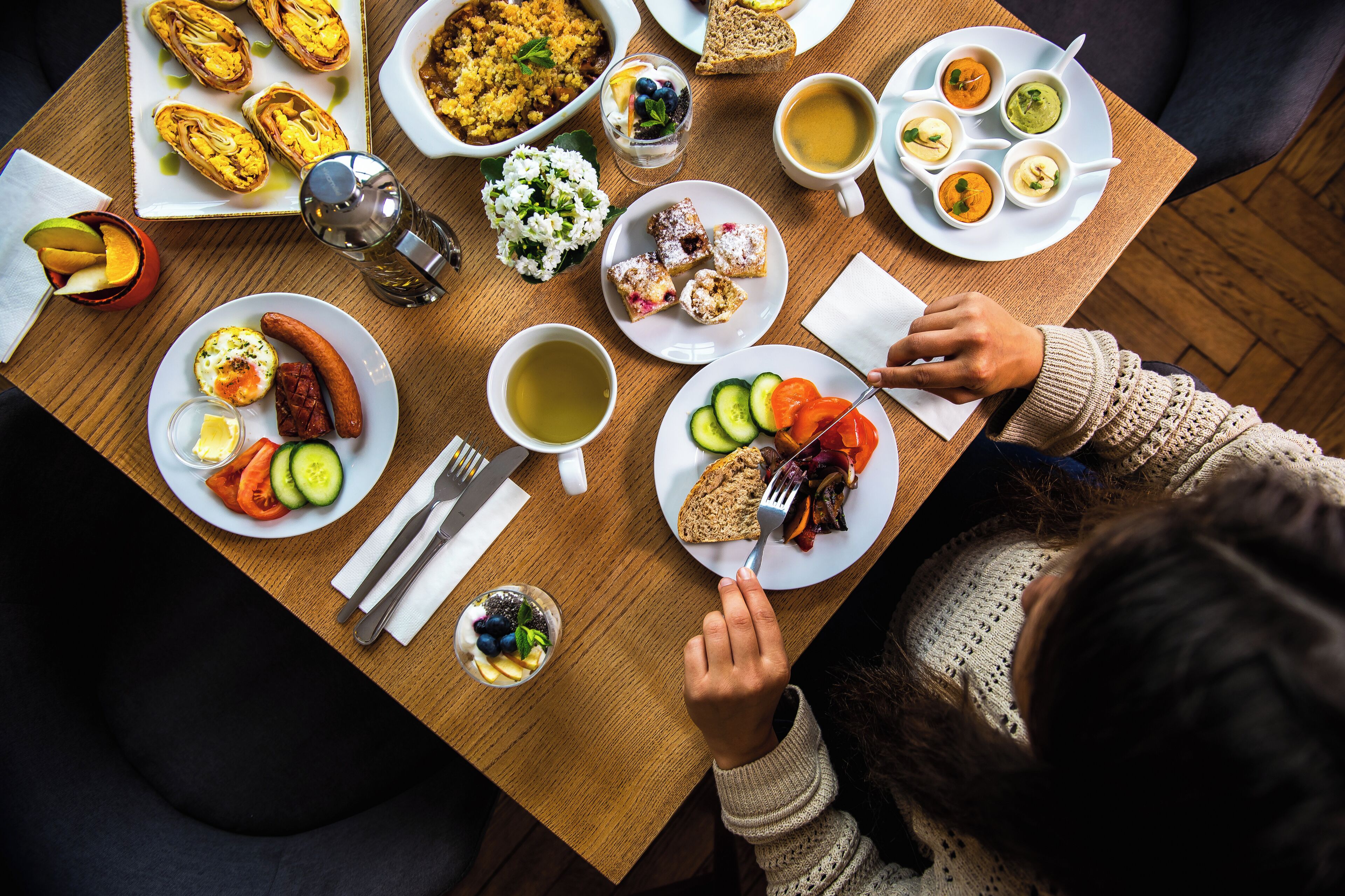 Una mesa de comedor con diversos platos, incluyendo pan, verduras y una salchicha caliente.